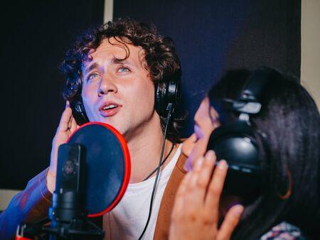 Two young singers performing song in record studio.Professional musician duet recording new album CD.Beautiful couple working and singing near microphone together.の写真素材