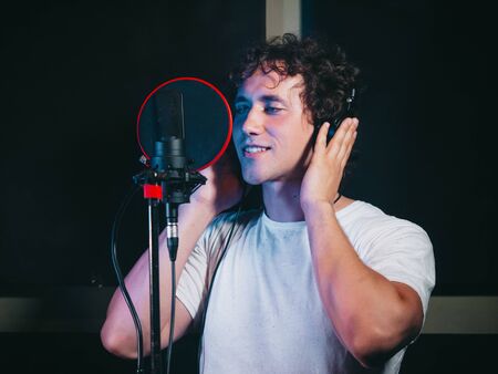Male vocal artist with curly hair singing alone. Young handsome singer man emotionally writing song in the studio. Recording new melody or album.の写真素材