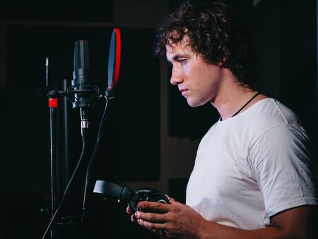 Young handsome singer man puts on headphones in the studio. Recording new melody or album. Male vocal artist with curly hair preparing for working.の写真素材