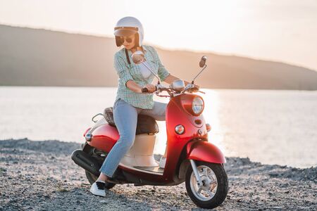 Cute girls portrait. Woman in helmet and sunglasses sitting on red retro motor bicycle at sunset...