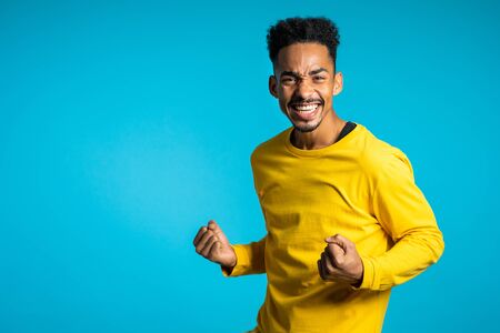 Man shows yes gesture of victory,he achieved result, goals. Surprised excited happy african guy on blue background. Copy space.の写真素材