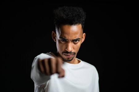 Young serious handsome african man with closed fist pointing to camera. Boxing, anger, aggressive emotions, fighting concept. Black studio backgroundの写真素材