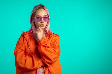 Cheerful odd girl in blue studio. Smiling woman with nose piercing, sunglasses. Vibrant colorful...