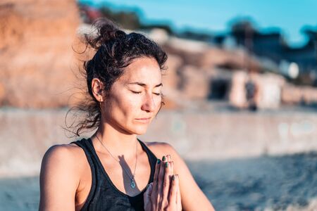 Pleasant woman makes greeting to the sun at sunrise on sea coast. Hands in namaste. Yoga, meditation, gratitude, healthy lifestyle concept.の写真素材