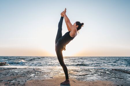 Young woman with curly hair in black costume practicing yoga at sunrise light, minimalist scene....