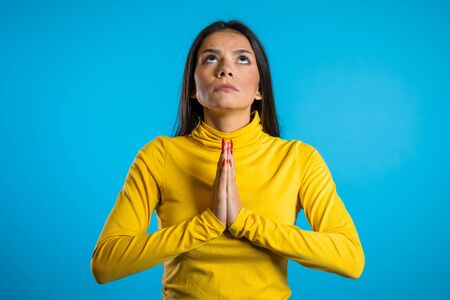 Attractive woman with long hair praying over blue background. Pretty girl begging someone. Hope concept.の写真素材