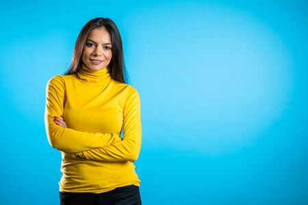 Copy space. Beautiful cheerful mixed race woman in yellow clothing smiling to camera over blue wall background. Cute hispanic girls portrait.の写真素材