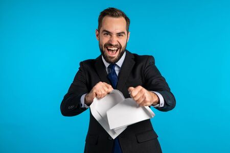 Serious businessman tearing contract in pieces. Angry furious male office worker throwing crumpled paper, having nervous breakdown at work, screaming in anger, stress management.の写真素材