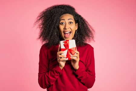 Beautiful african american woman received gift box with bow. She is happy and flattered by attention. Girl on studio background.の写真素材