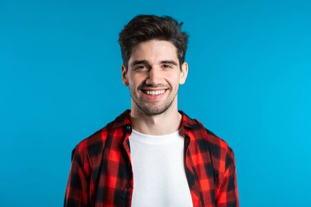 Handsome european man with trendy hairdo in red plaid wear on blue studio background. Cheerful guy smiling and looking to camera.の写真素材