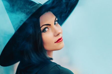 Portrait of woman as witch in black on blue fog, smoke background. Fairy tale concept, halloween,...