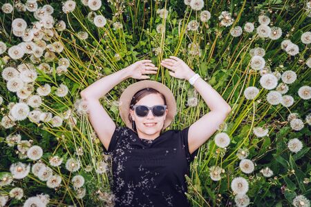 Young beautiful girl in sunglasses lies in dandelion field and looks to the sky. Top view.の写真素材