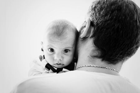 Portrait of cute baby boy on fathers shoulder and looking to camera. Childhood, fatherhood, family...