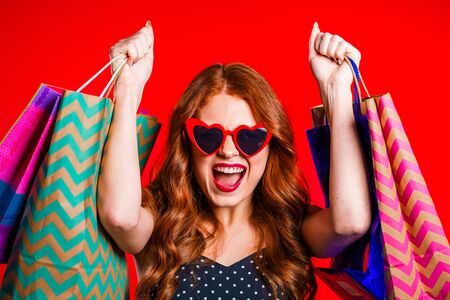 Happy retro styled young woman with red hair and paper bags after shopping isolated on studio...