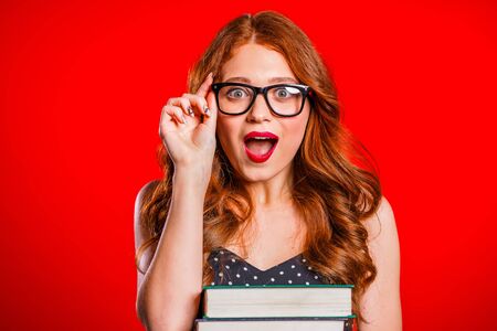 Surprised excited female student on red background in studio holds stack of university books from...