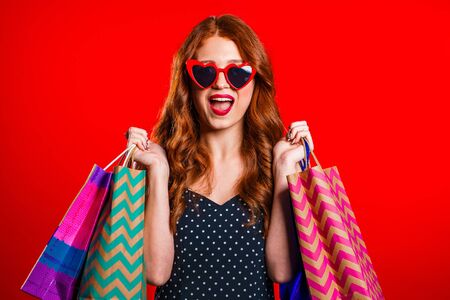 Happy retro styled young woman with red hair and paper bags after shopping isolated on studio background. Seasonal sale, purchases, spending money on gifts conceptの写真素材
