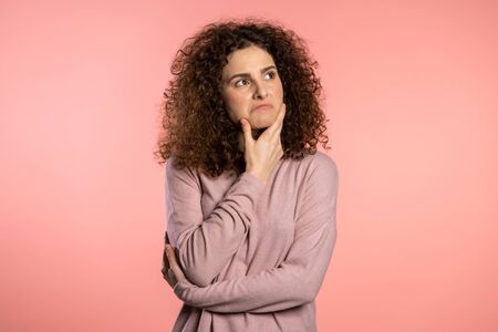 Thinking woman looking up and around on pink background. Worried contemplative face expressions. Pretty curly girl modelの写真素材