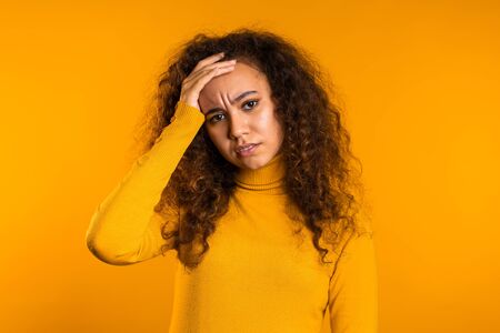 Young upset woman with curly hair having headache, studio portrait. Girl putting hands on head,...