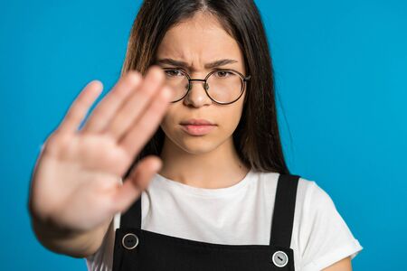 pretty brunette woman disliking and rejecting gesture by stop sign. Portrait of young successful confident girl isolated on blue backgroundの写真素材