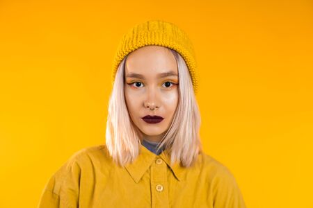 Young woman in total trendy yellow look. Portrait of beautiful punk girl with dark make-up and nose piercing on studio background.の写真素材