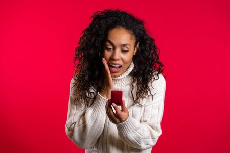 Amazed african american young woman holding small jewelry box with proposal