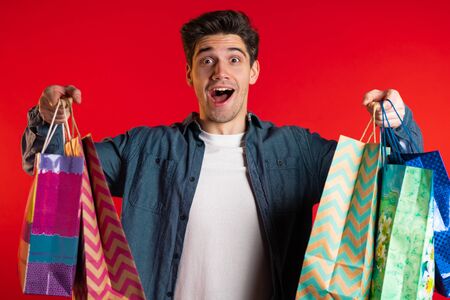 Handsome young man holds shopping paper bags on red studio backgroundの写真素材