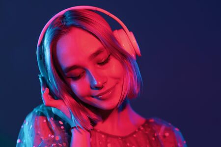 Mysterious hipster teenager listening to music with headphones. Portrait of millennial pretty girl with short hairstyle with neon light. Dyed blue and pink hair.の写真素材