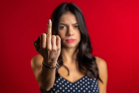 Young pretty woman on red background showing middle finger - gesture of fuckの写真素材