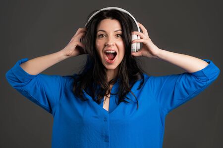 Attractive european adult woman with long hair dancing with headphones on grey studio background. Cute ladys portrait. Music, radio, happiness, freedom, youth concept.の写真素材