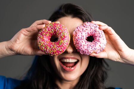 Portrait of cheerful beautiful woman dancing with sweets colorful donuts isolated on grey studio background. Concept of joy, food, lifestyleの写真素材