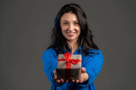 Excited adult woman received gift box with bow. She is happy and flattered by attention. Mature lady dancing with present on grey background. Studio portraitの写真素材