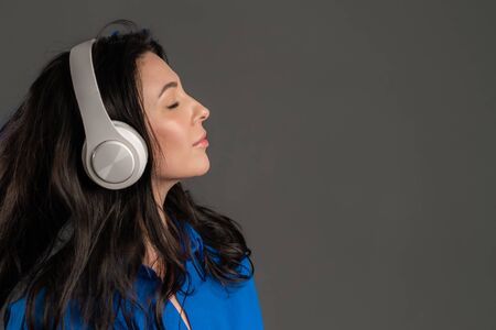 Attractive european adult woman with long hair dancing with headphones on grey studio background. Cute ladys portrait. Music, radio, happiness, freedom, youth concept.の写真素材