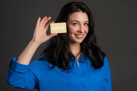 Successful pretty adult woman look to camera and showing unlimited gold credit card on grey studio background.の写真素材