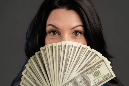 Satisfied happy excited adult woman showing money - U.S. currency dollars banknotes on grey wall. Symbol of success, gain, victory.の写真素材