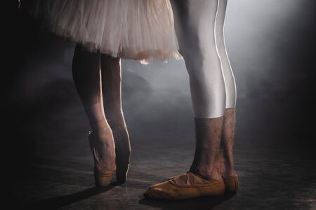 Close up of ballet couple of dancers as they practices exercises on dark stage or studio. Womans and mans feet in pointe shoes. Ballerina shows classic ballet pas. Slow motion. Flare shot.の写真素材