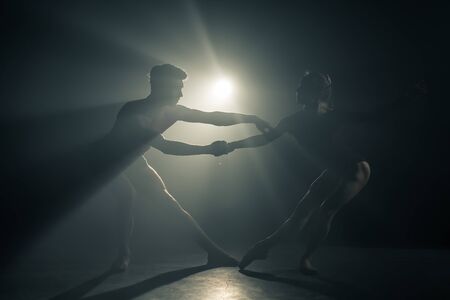 Professional ballet couple dancing in spotlights smoke on big stage. Beautiful young woman and man on floodlights background. Emotional duet performing choreographic art.の写真素材