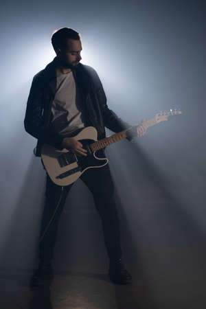 Odessa, Ukraine - October 31, 2019. Rock guitarist man in leather jacket in smoky studio or stage masterfully playing electric guitar. View of musician in the spotlight.のeditorial素材