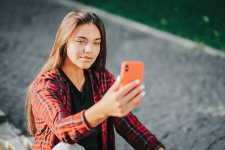 Young pretty woman sitting in green park and using mobile phone. Surfing internet, social networks, internet concept.の写真素材