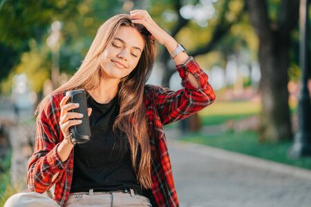 Modern trendy girl listening to music by wireless portable speaker.Young beautiful american woman enjoying,dancing in park.の写真素材