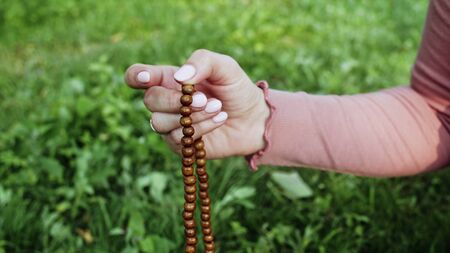 Woman lit hand close up counts rosary - malas strands of gemstones beads used for keeping count during mantra meditations. Girl sits on summer nature.の写真素材