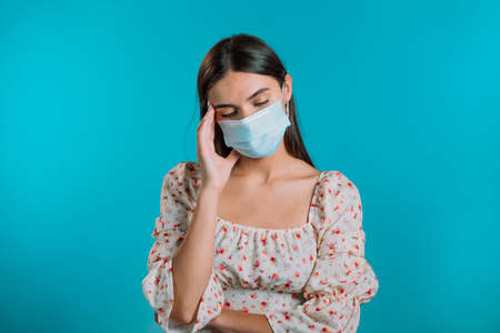 Girl in medical mask is tired, bored of work or studying, she disappointed, helpless. Frustrated european woman over blue wall background.の写真素材