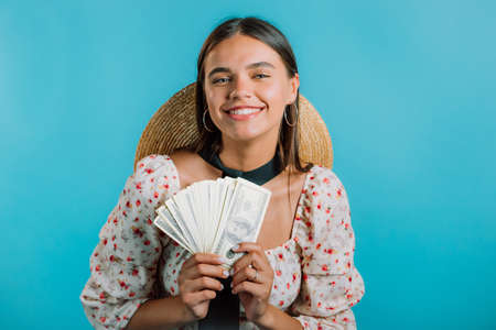 Amazed happy excited woman with money - U.S. currency dollars banknotes on blue wall. Symbol of...