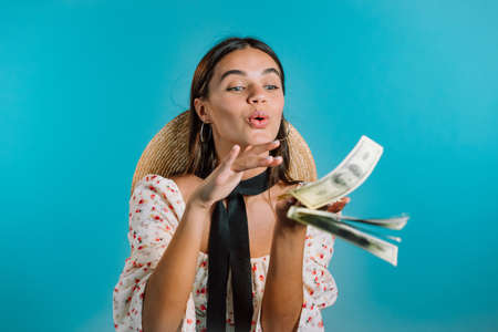 Pretty woman with happy face scatters, waste money. Girl overspend US currency. Lady is flush with dollars on blue studio background .の写真素材