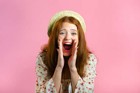 Woman with red hair very glad, she screaming loud. Woman trying to get attention. Concept of sales, profitable offer. Excited happy lady on pink studio background.の写真素材
