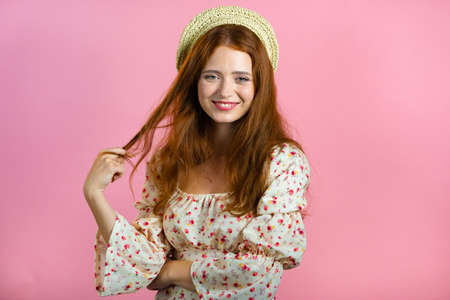 Young woman with long red wavy and shiny hairstyle looking to camera, flirting. Beautiful model girl demonstrate her elegant volume hair. Pink studio background.の写真素材