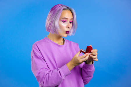 Attractive young woman with dyed colorful hair holding small jewelry box with proposal diamond ring...