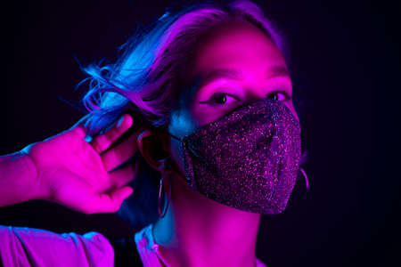 Young beautiful fashionable woman in protective mask with rhinestones dancing in night club. Neon colorful light. Close-up portrait of fashion model.の写真素材
