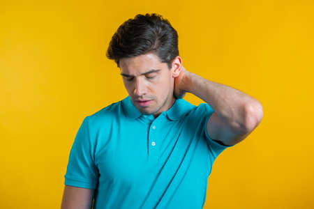 Young man having pain in neck, studio portrait. Guy putting hands on throat, isolated on yellow background. Concept of problems, medicine, illnessの写真素材
