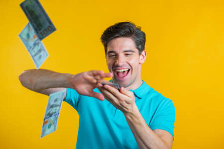 Man with a happy face scatters money. People overspend US currency. The man is flush with dollars on yellow studio background.の写真素材