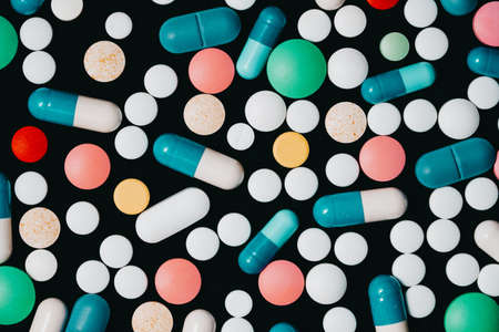 Pharmacy theme. Multicolored Isolated Pills and Capsules on Black Surface. Vitamins, drugs concept....